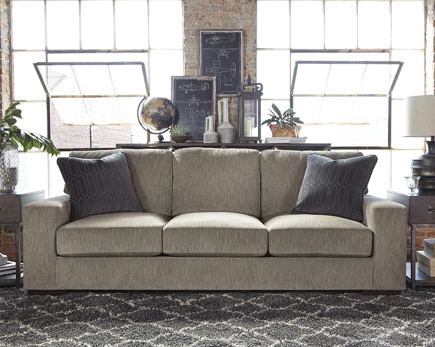 Gray track arm syled sofa with dark pillows and a black chevron rug underneath. 